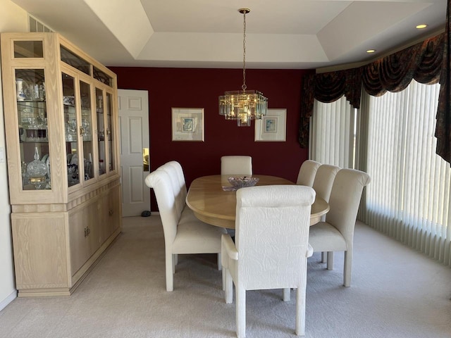 carpeted dining area with a chandelier and a tray ceiling