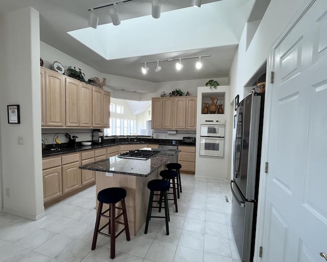 kitchen with light brown cabinets, a kitchen island, rail lighting, stainless steel appliances, and a kitchen bar