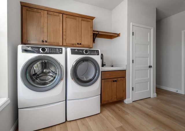 clothes washing area with cabinets, washing machine and dryer, light wood-type flooring, and sink