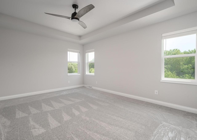 carpeted empty room with a raised ceiling and ceiling fan