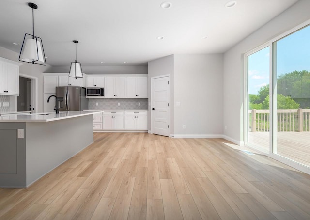 kitchen featuring hanging light fixtures, tasteful backsplash, light hardwood / wood-style floors, white cabinetry, and stainless steel appliances