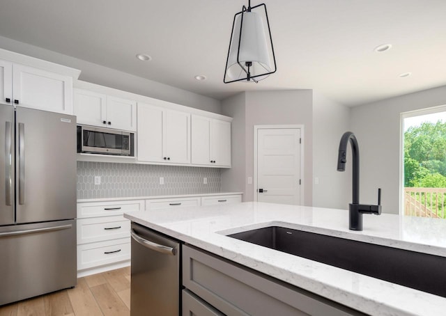 kitchen featuring tasteful backsplash, white cabinets, hanging light fixtures, and appliances with stainless steel finishes