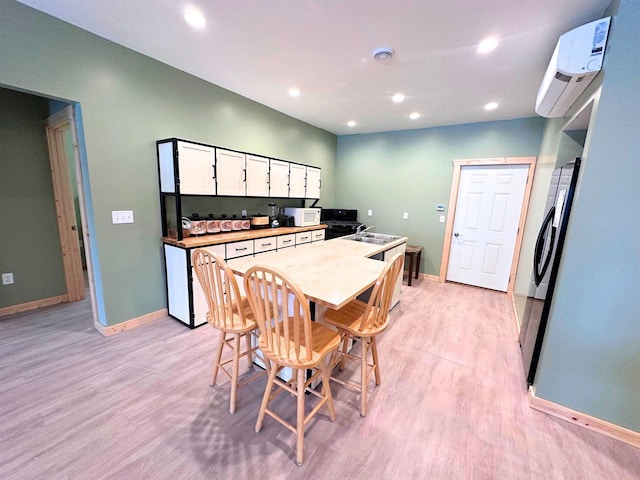 kitchen with white cabinets, light hardwood / wood-style floors, stainless steel refrigerator, and an AC wall unit