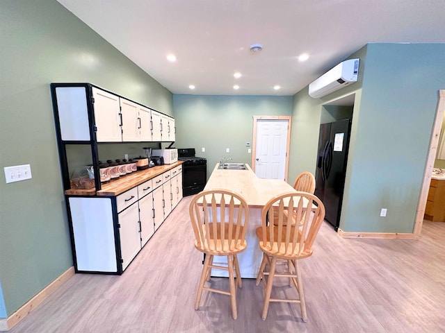 kitchen with black appliances, white cabinets, sink, light wood-type flooring, and a wall unit AC