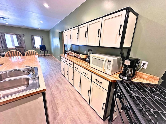 kitchen with range with electric cooktop, sink, light hardwood / wood-style flooring, butcher block countertops, and white cabinets