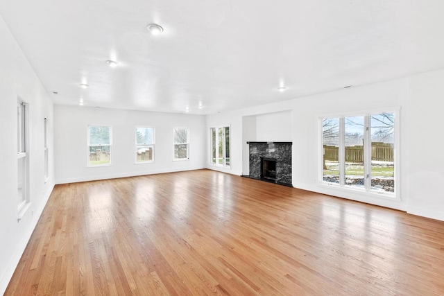 unfurnished living room with a premium fireplace, light hardwood / wood-style flooring, and a healthy amount of sunlight