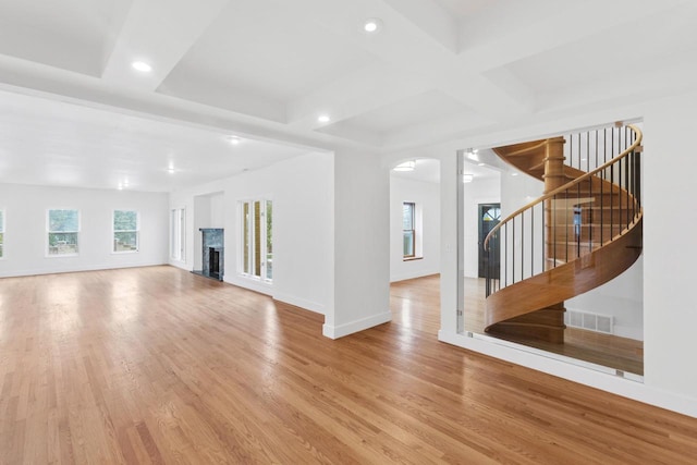 unfurnished living room featuring a wealth of natural light, coffered ceiling, beam ceiling, and light wood-type flooring