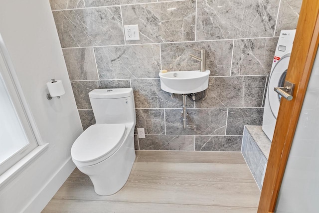 bathroom with tile walls, sink, hardwood / wood-style flooring, washer / dryer, and toilet