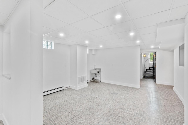 basement featuring a drop ceiling and baseboard heating