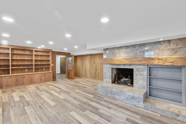 unfurnished living room featuring built in features, a stone fireplace, and light hardwood / wood-style flooring