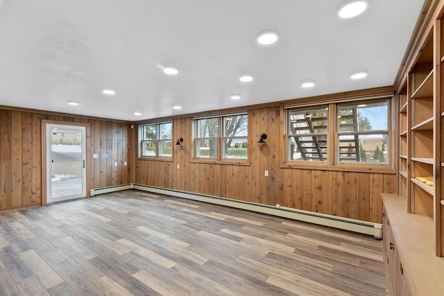 unfurnished room with wood walls, a baseboard radiator, and light wood-type flooring