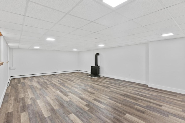 basement featuring hardwood / wood-style floors, a paneled ceiling, and a wood stove