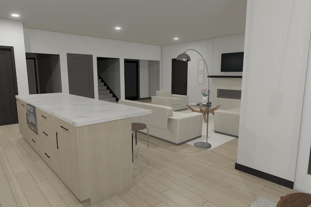 kitchen with a kitchen island, light stone counters, a breakfast bar, and light wood-type flooring