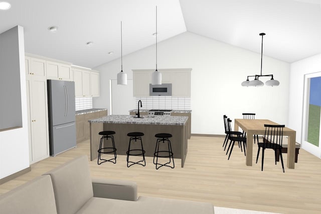 kitchen featuring stainless steel refrigerator, light hardwood / wood-style flooring, hanging light fixtures, a kitchen island with sink, and light stone counters