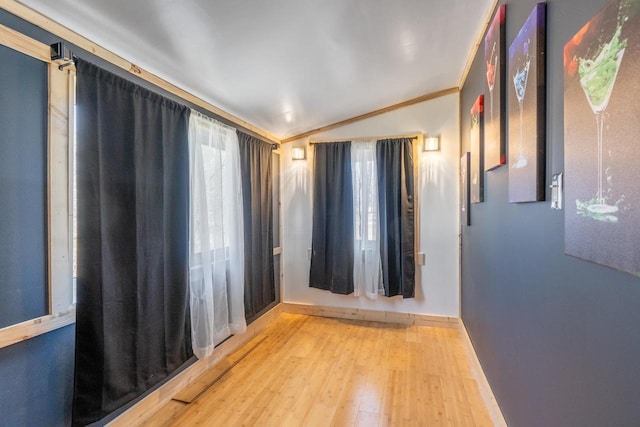 empty room with crown molding, light hardwood / wood-style floors, and vaulted ceiling