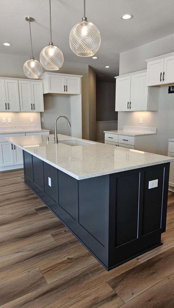 kitchen featuring dark hardwood / wood-style flooring, pendant lighting, a spacious island, sink, and white cabinetry