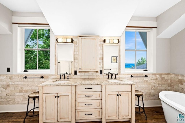 bathroom with tile walls, dual bowl vanity, hardwood / wood-style floors, and a bathtub