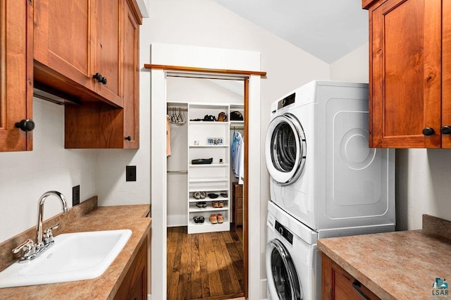 laundry room with stacked washer and clothes dryer, cabinets, wood-type flooring, and sink