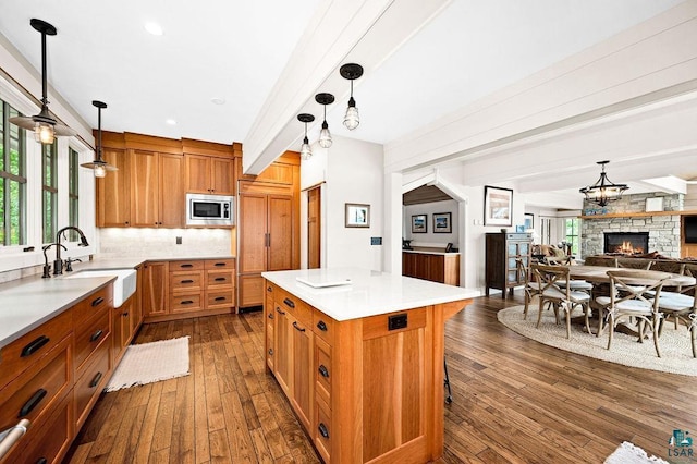 kitchen with hanging light fixtures, dark hardwood / wood-style floors, built in appliances, and a stone fireplace