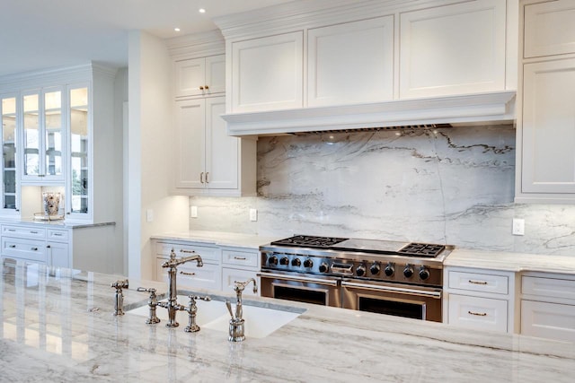 kitchen featuring backsplash, light stone counters, white cabinetry, and range with two ovens