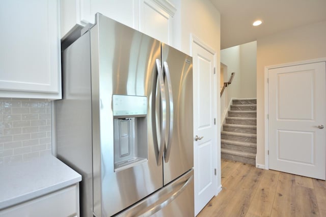 kitchen with tasteful backsplash, stainless steel fridge, white cabinetry, and light hardwood / wood-style floors