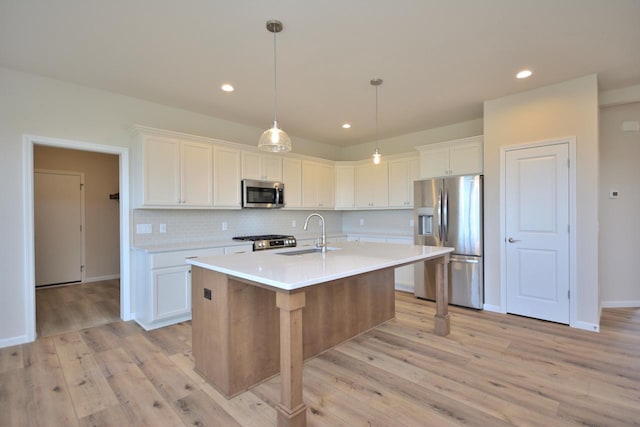 kitchen with appliances with stainless steel finishes, decorative light fixtures, white cabinetry, sink, and a kitchen island with sink