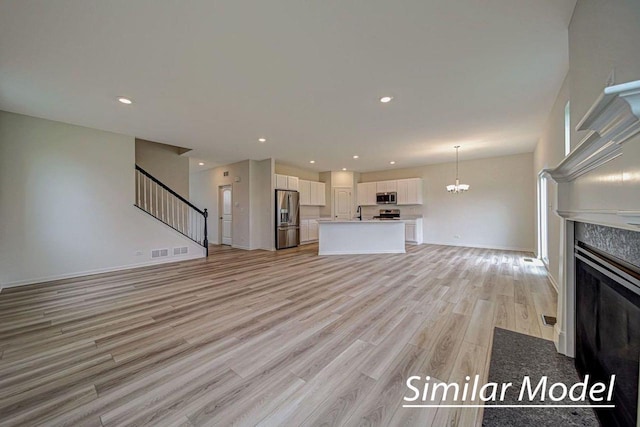 unfurnished living room with a notable chandelier, light hardwood / wood-style floors, and a premium fireplace