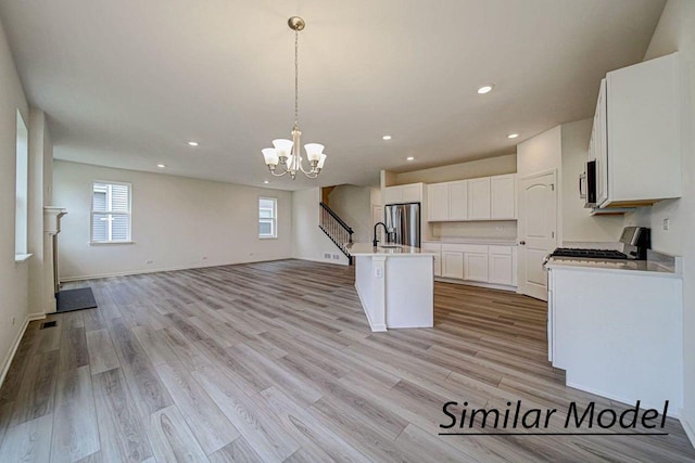 kitchen with stainless steel appliances, a notable chandelier, pendant lighting, a center island with sink, and white cabinets