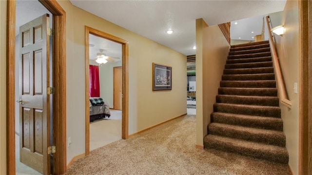 stairs featuring light carpet and ceiling fan