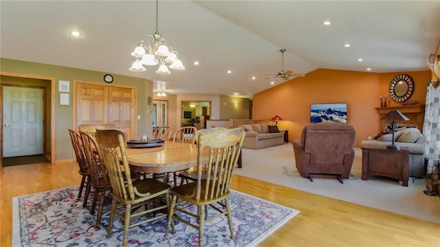 dining area featuring ceiling fan with notable chandelier, light colored carpet, and lofted ceiling