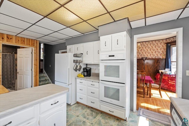 kitchen featuring a paneled ceiling, white cabinets, wooden walls, and white appliances