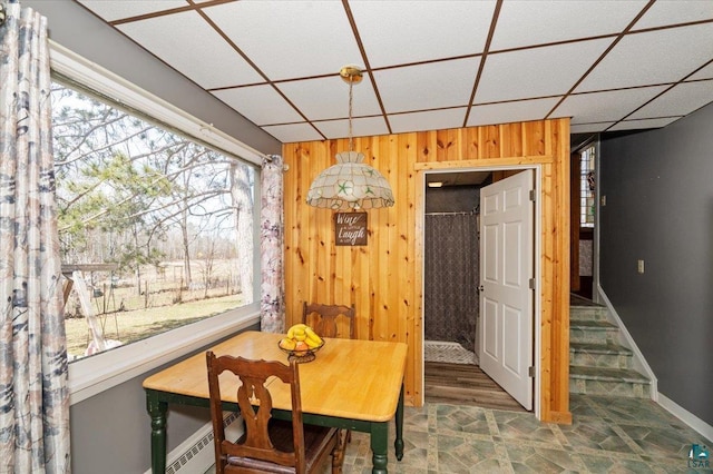 dining area featuring a wealth of natural light, a drop ceiling, and wood walls