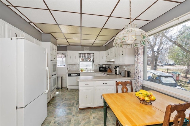 kitchen with a paneled ceiling, a wealth of natural light, white cabinets, and white appliances