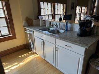 kitchen with white cabinets, light wood-type flooring, light stone countertops, sink, and stainless steel dishwasher