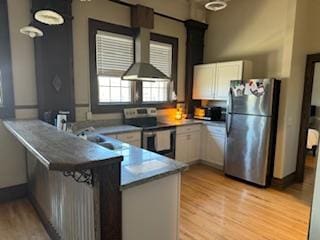 kitchen with white cabinets, light hardwood / wood-style flooring, wall chimney range hood, and appliances with stainless steel finishes