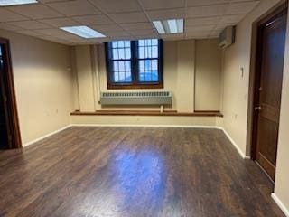 spare room featuring dark hardwood / wood-style floors, a drop ceiling, and radiator