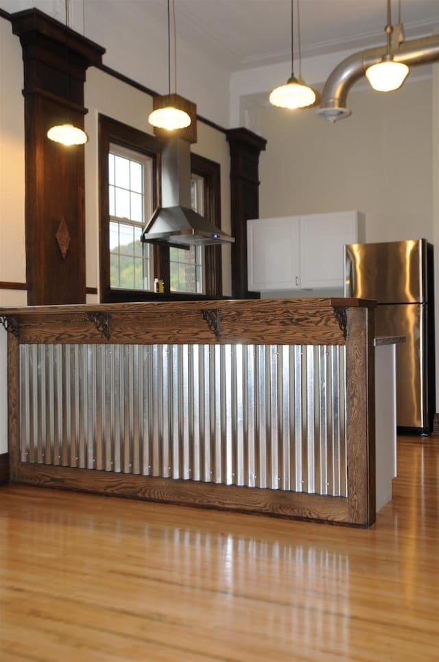 kitchen with hanging light fixtures, light hardwood / wood-style flooring, and wall chimney exhaust hood