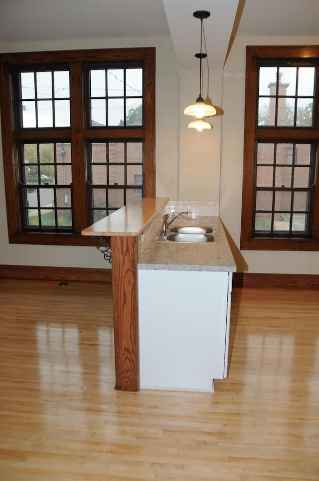 kitchen with kitchen peninsula, decorative light fixtures, light hardwood / wood-style floors, a healthy amount of sunlight, and sink