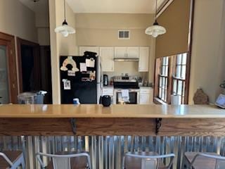 kitchen with stainless steel stove, a kitchen bar, white cabinetry, black fridge, and pendant lighting