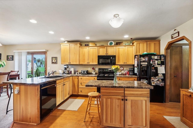 kitchen with a center island, black appliances, a kitchen bar, and light wood-type flooring