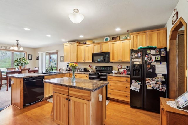 kitchen with decorative light fixtures, black appliances, sink, a kitchen island, and light hardwood / wood-style floors