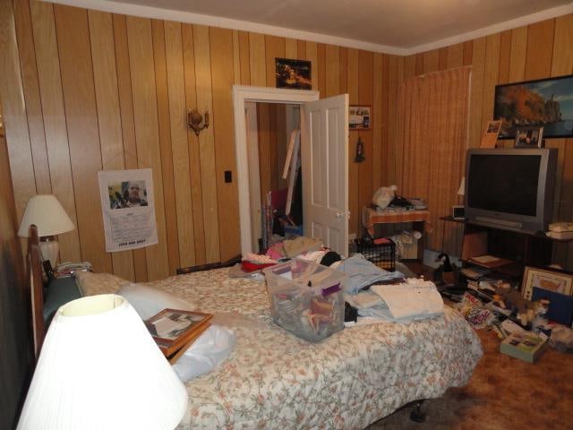 bedroom featuring crown molding, carpet floors, and wooden walls