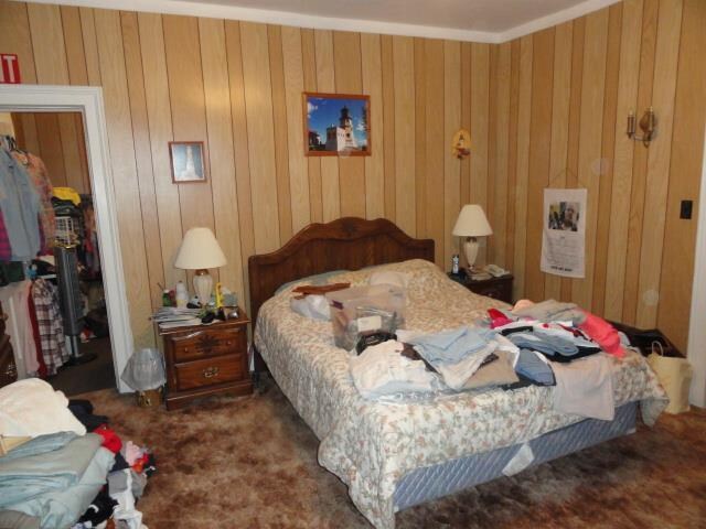 bedroom featuring crown molding, carpet floors, and wooden walls