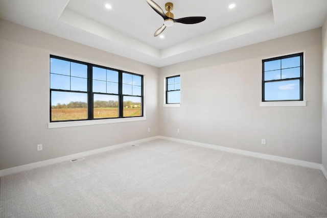 carpeted spare room with ceiling fan and a tray ceiling