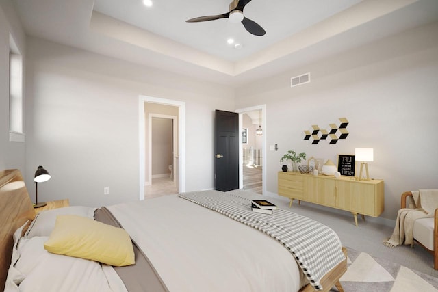 carpeted bedroom featuring ceiling fan, a raised ceiling, and ensuite bathroom