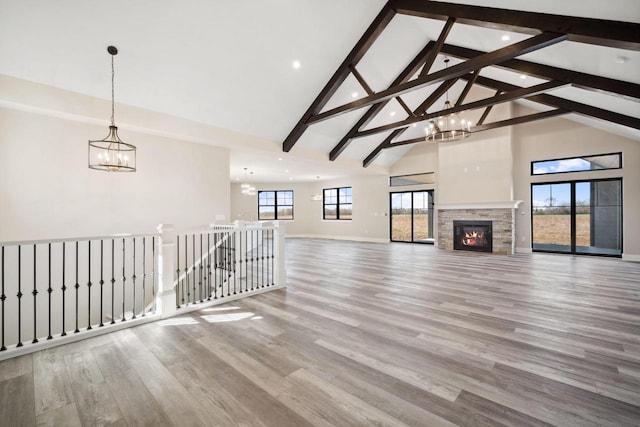 unfurnished living room with wood-type flooring, high vaulted ceiling, beamed ceiling, and a stone fireplace