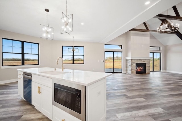 kitchen with light hardwood / wood-style flooring, white cabinetry, a center island with sink, sink, and black microwave