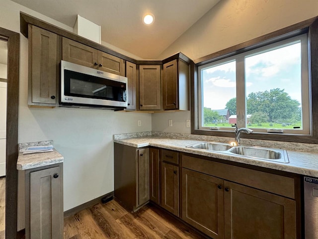 kitchen with sink, dark brown cabinets, stainless steel appliances, wood-type flooring, and vaulted ceiling