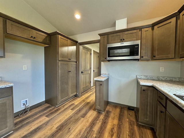 kitchen with dark brown cabinetry, lofted ceiling, dark hardwood / wood-style flooring, and light stone countertops