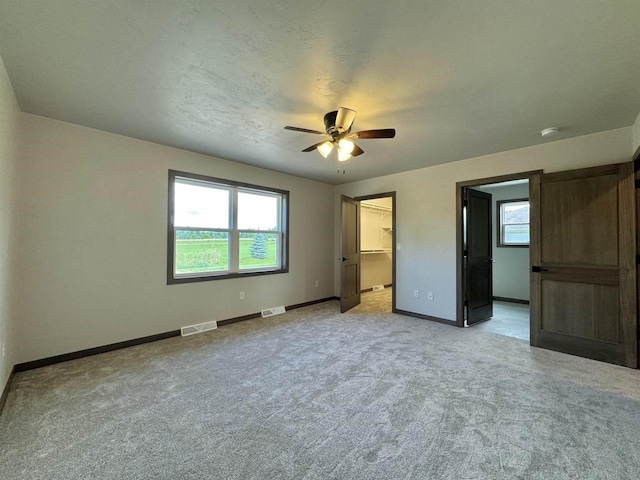 unfurnished bedroom featuring multiple windows, a spacious closet, light colored carpet, and ceiling fan